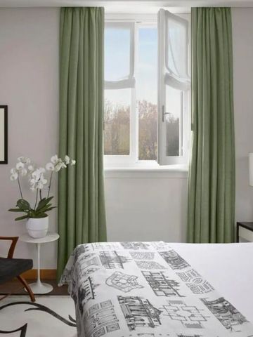 Modernes und helles Zimmer mit großen Fenstern und grünen Vorhängen