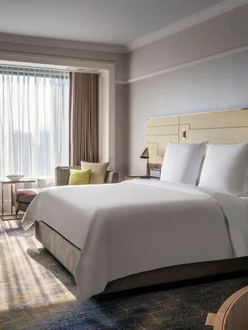 Helles Zimmer mit großem Bett und Sitzbereich vor einem großen Fenster