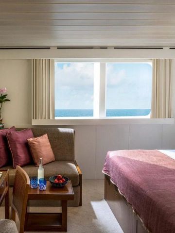 Helles Hotelzimmer mit Meerblick aus dem großen Fenster und gemütlicher Sitzecke