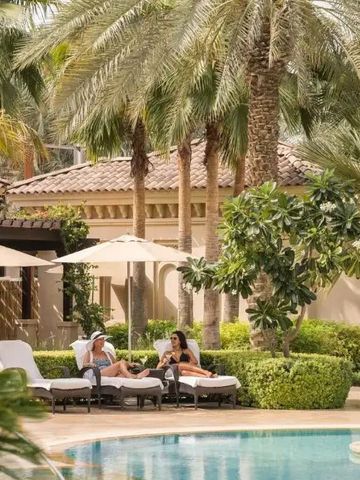 Poolbereich mit Liegestühlen umgeben von Palmen und grüner Landschaft