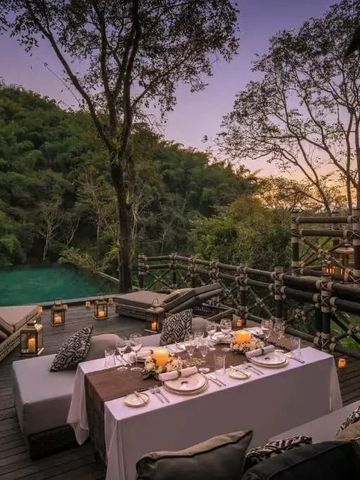 Romantisches Abendessen auf einer Terrasse mit Blick auf Dschungel und Pool im Sonnenuntergang.