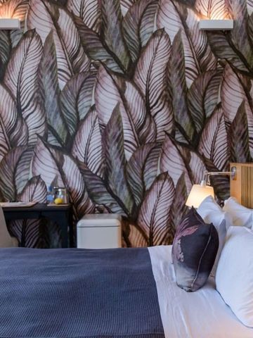 Zimmer mit auffälliger Blatt-Tapete und gemütlichem Bett.