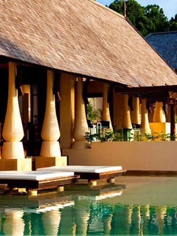 Elegantes Resortgebäude am Wasser mit traditionellen Designelementen und Sonnenliegen