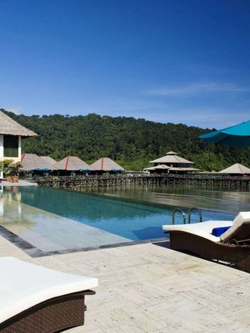Infinity-Pool mit Blick auf grüne Hügel und strohgedeckte Hütten unter blauem Himmel.