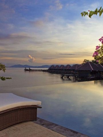 Sonnenuntergang über dem Meer mit luxuriösen Wasservillen und blühenden Pflanzen.