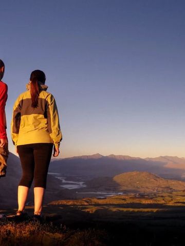 Zwei Wanderer auf einem Berg mit weitem Blick über Bergkette und Tal im Sonnenuntergang