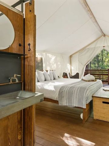 Zeltinterieur mit Waschbecken und Bett neben einer Veranda.