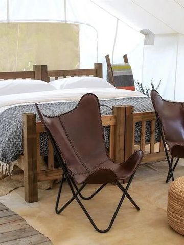 Zelt mit Holzbett und eleganten Ledersesseln.