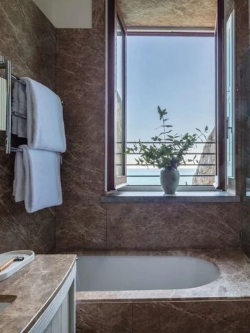 Badezimmer mit Marmorwänden und Aussicht aufs Meer durch ein offenes Fenster.