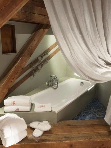 Badewanne in gemütlicher Nische mit Holzbalken und cremefarbenem Vorhang