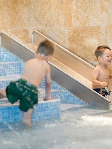 Kinder spielen lachend auf einer Wasserrutsche im Wellnessbereich