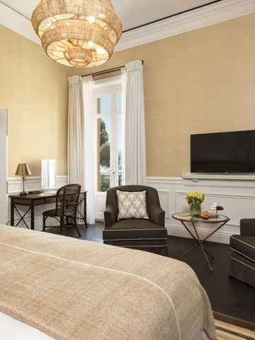 Elegantes Hotelzimmer mit großem Bett, Sesseln und einem modernen Kronleuchter.