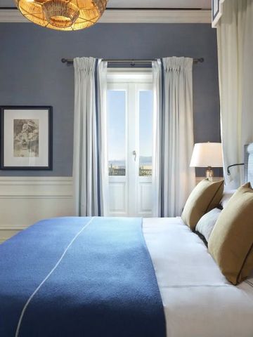 Modernes Hotelzimmer mit blauem Bett, großen Fenstern und Blick auf das Meer.