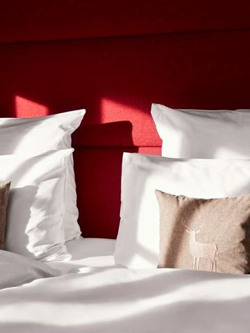 Doppelbett mit weißer Bettwäsche und roter Wand im Hintergrund