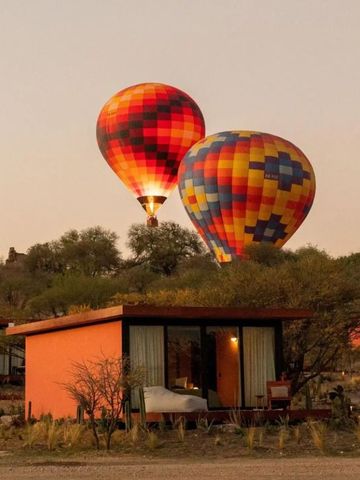 Heißluftballons über einem modernen Bungalow in wüstenähnlicher Landschaft