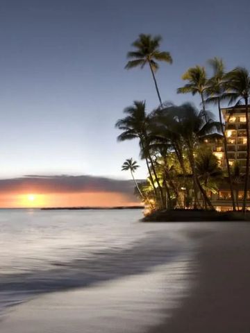 Strand bei Sonnenuntergang mit Palmen und beleuchtetem Hotel