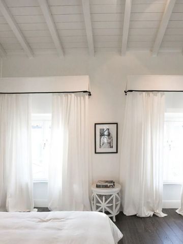 Lichtdurchflutetes Zimmer mit Holzbalkendecke und weißen Vorhängen