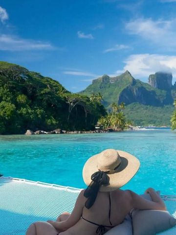 Frau entspannt auf Netz über türkisblauem Wasser mit Blick auf üppige Vegetation und Berge