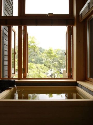 Holz-Indoor-Onsen mit Blick ins Grüne durch große Fenster.