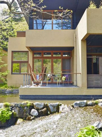 Villa mit Terrasse an einem kleinen Bach in grüner Umgebung.