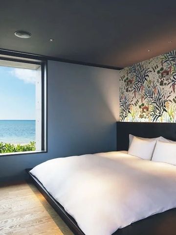 Zimmer mit großem Bett und Fenster mit Meerblick. Floral dekorierte Wand.