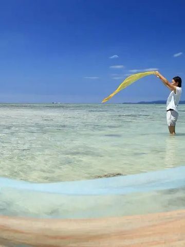 Person steht im klaren Wasser des Meeres mit einem Tuch in der Hand unter blauem Himmel
