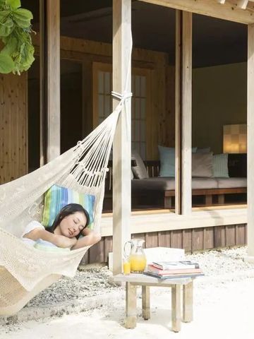 Person in Hängematte vor einer Villa mit Getränken auf einem Tisch daneben