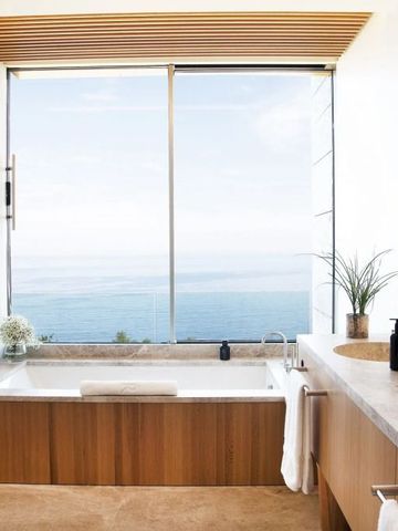 Großes Badezimmer mit Badewanne und Panoramafenster mit Meerblick