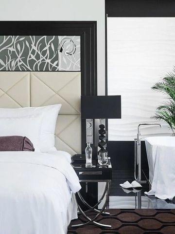 Schlafzimmer mit weißem Bett und stilvollem Badezimmer im Hintergrund.