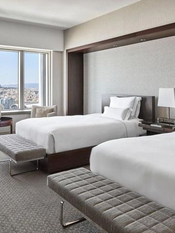 Helles Hotelzimmer mit zwei Einzelbetten und Panoramafenster zeigt Stadtansicht