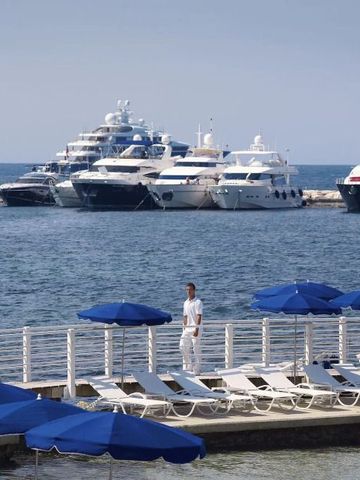 Yachten im Hafen vor einem Hotelstrand mit weißen Liegen