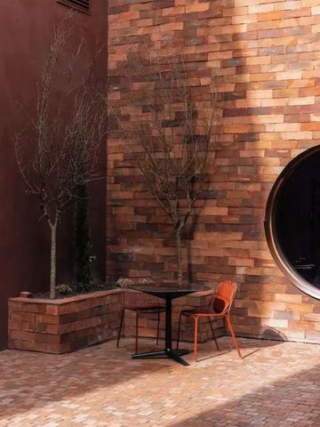Terrasse mit Backsteinwand, Tisch, Stühlen und minimalistischer Dekoration.