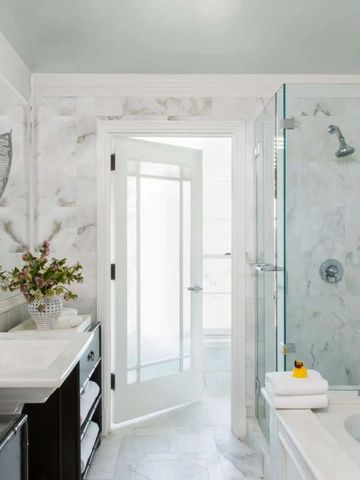 Elegantes Badezimmer mit Marmorwänden, Badewanne und floralem Arrangement.