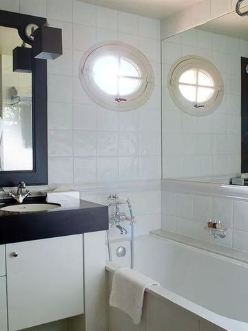 Helles Badezimmer mit Badewanne und zwei runden Fenstern