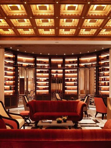 Elegante Hotelbar mit samtroten Sofas und beleuchteten Regalen in warmem Ambiente.