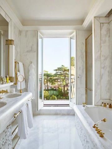 Badezimmer mit Marmor und großen Fensterblick auf eine Terrasse.