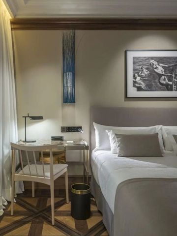 Elegantes Hotelzimmer mit Schreibtisch und Wandkunst neben einem gemütlichen Bett