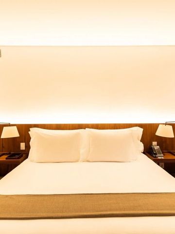 Nahaufnahme eines großen luxuriösen Hotelbetts mit warmem Licht und Holzakzenten.