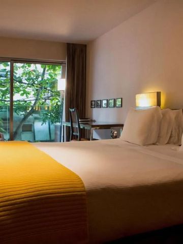 Gemütliches Hotelzimmer mit Doppelbett und Blick auf einen grünen Baum im Hotel Fasano Rio de Janeiro.