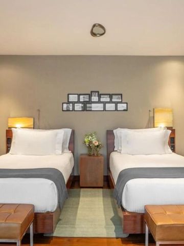 Zwei Einzelbetten in einem stilvollen Hotelzimmer mit dekorativer Wand im Hotel Fasano Rio de Janeiro.