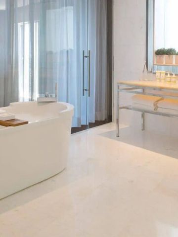 Weißes Badezimmer mit freistehender Badewanne und großem Fenster mit Vorhang.