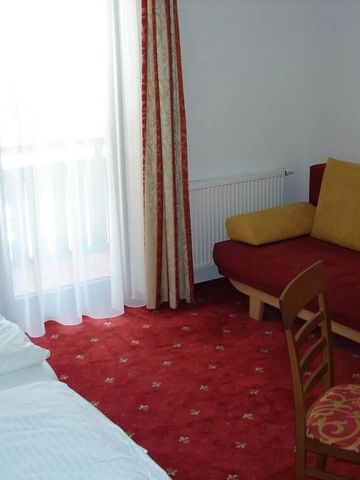 Zimmer mit rotem Teppich und gelbem Sofa, helle Vorhänge lassen Licht herein