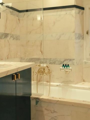 Luxuriöses Badezimmer in Marmoroptik mit goldenen Armaturen und Badewanne.
