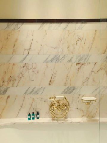 Elegantes Badezimmer mit Marmorwänden und goldenen Armaturen.