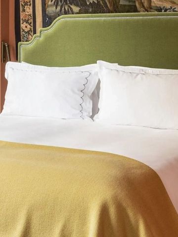 Bett mit grüner Kopfstütze und gelber Decke vor dekorativer Wand