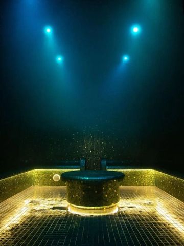 Stimmungsvolle Sauna mit goldenen Mosaikfliesen und blauer Beleuchtung.
