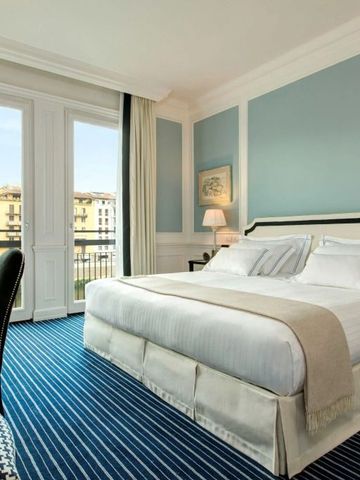 Elegant eingerichtetes Zimmer mit großem Bett, blauem Teppich und Stadtblick