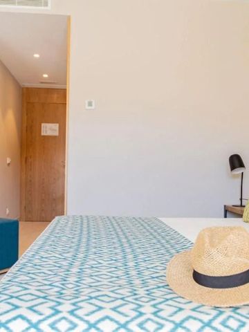 Helles Zimmer mit stilvoller Einrichtung und Strohhut auf dem Bett.