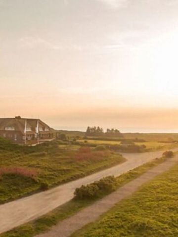 Weitläufige Landschaft mit Wiesen, einem Pfad und einem Gebäude im Sonnenuntergang