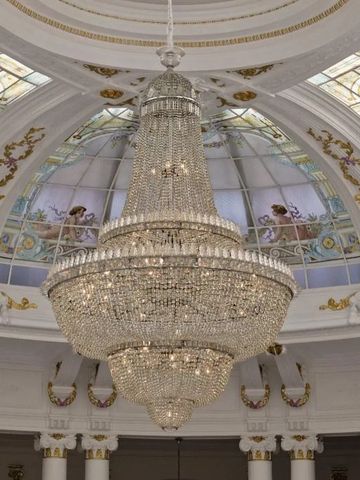 Prunkvoller Kronleuchter unter einem kunstvollen Glasdach in einem noblen Saal